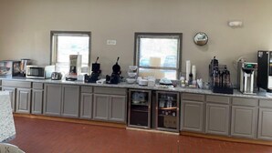 Una cocina con armarios grises, microondas, cafetera y refrigerador. Hay ventanas y un ventilador de techo.