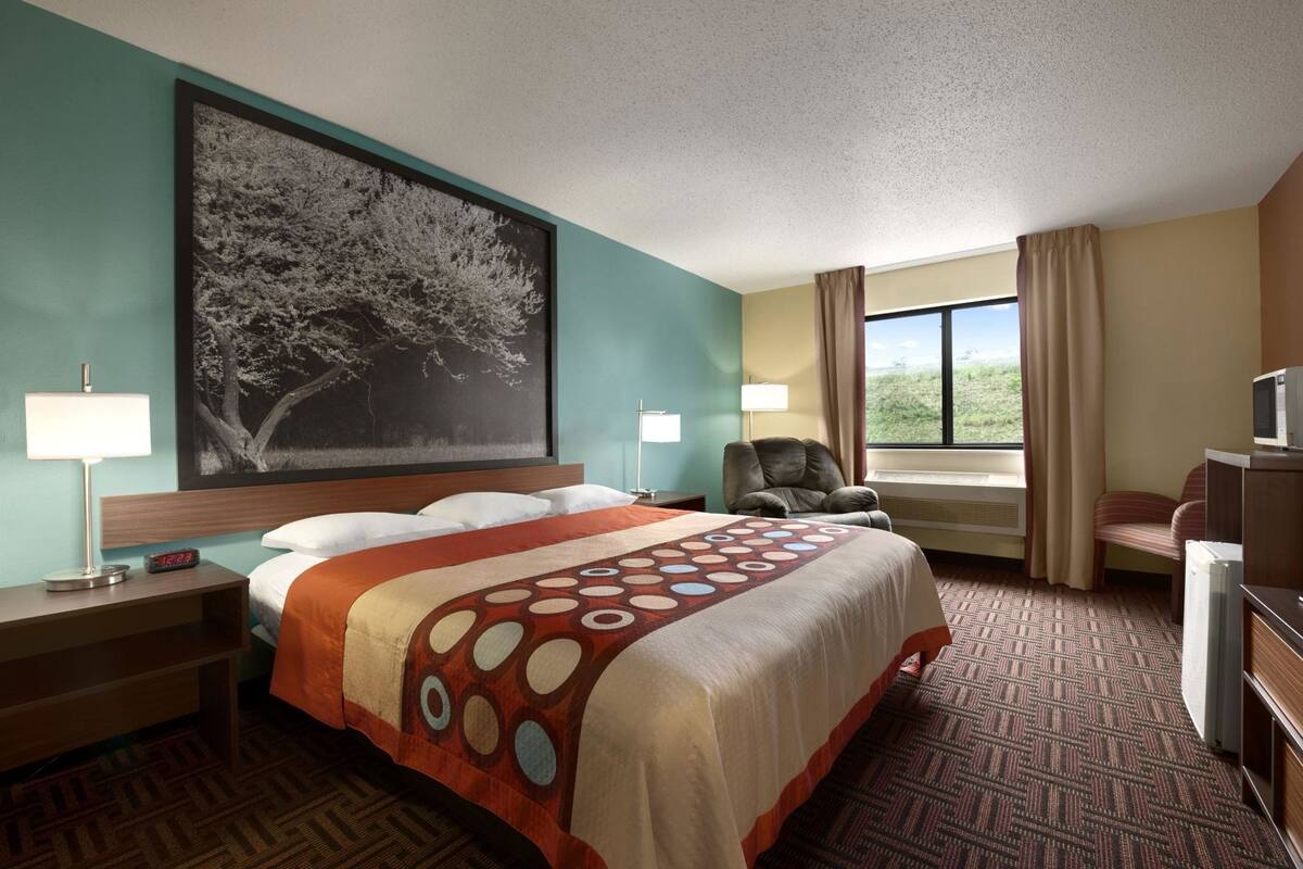A hotel room with a bed, two bedside tables, a chair, a TV, and a large window.