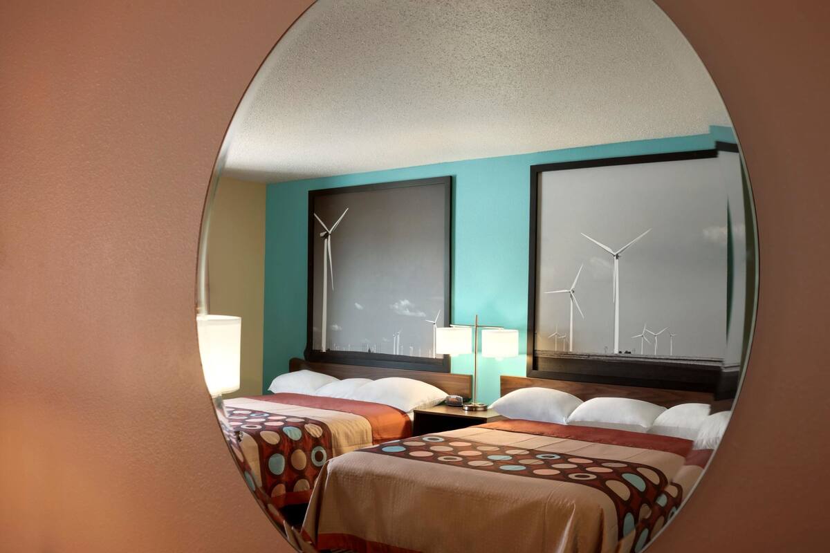 A hotel room with two beds, a large window with wind turbines, and a teal wall.