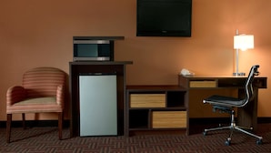 A hotel room with a desk, a chair, a television, a lamp, and a refrigerator. - Super 8 by Wyndham Peoria East (East Peoria)