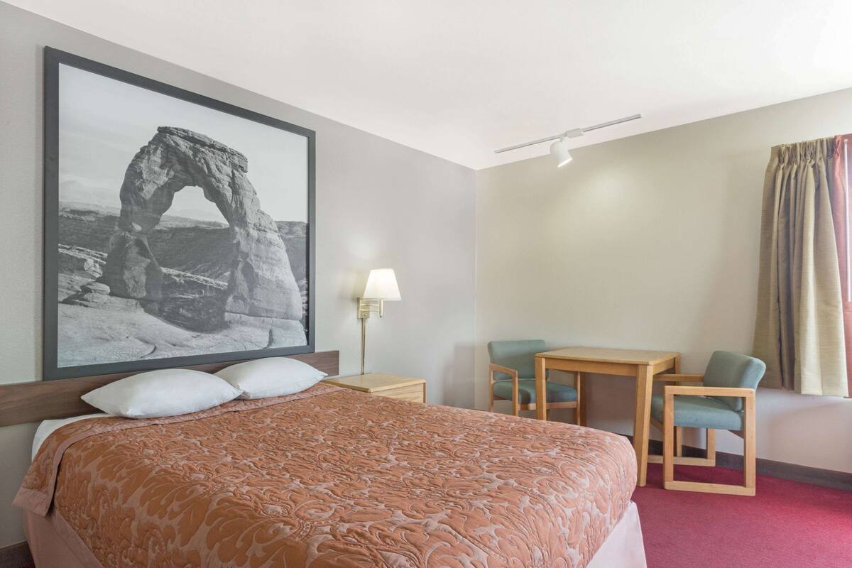 Una camera d'hotel con un letto grande, una scrivania con due sedie, una lampada e una fotografia incorniciata appesa al muro.