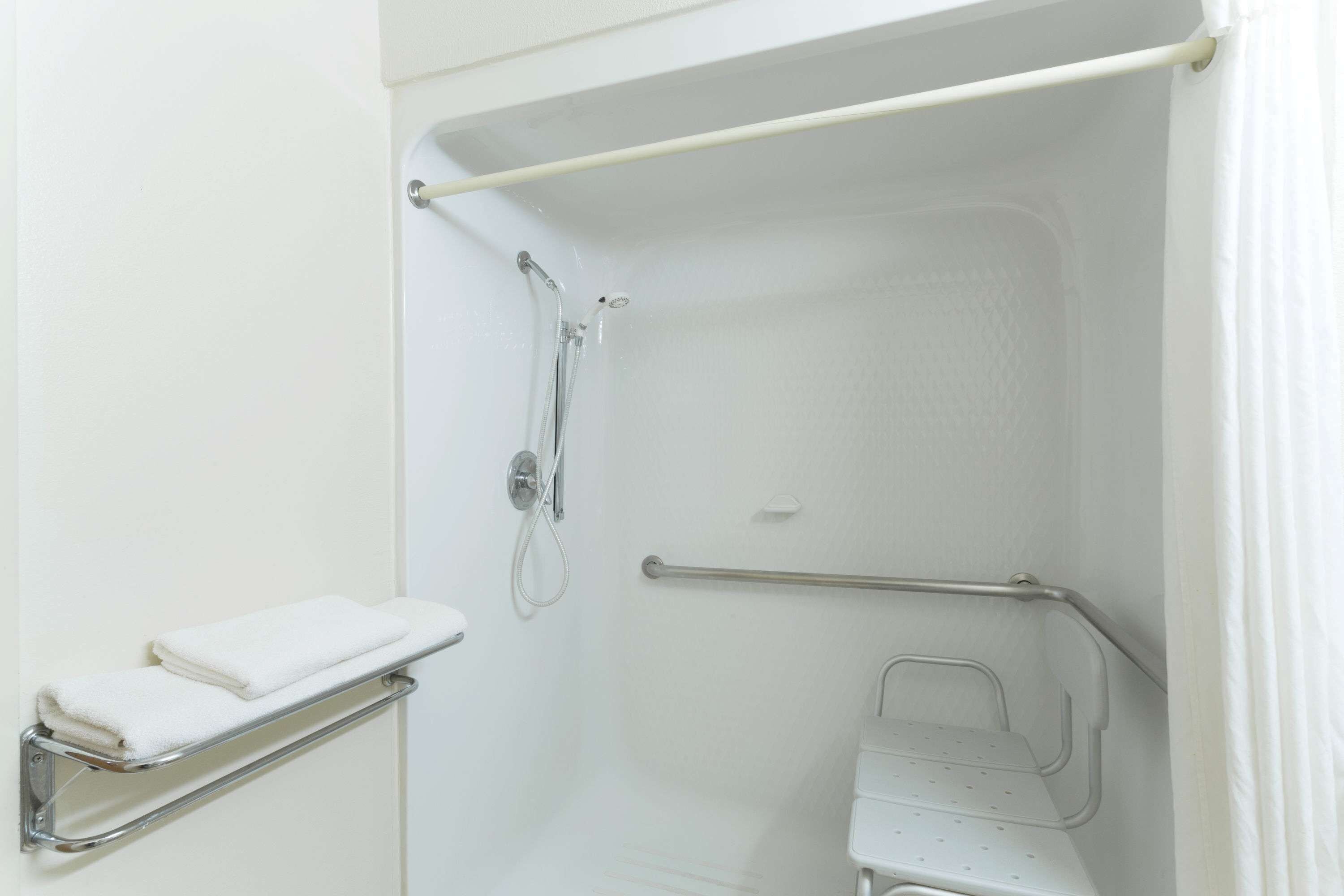 A white bathroom with a shower, a grab bar, and a towel rack.