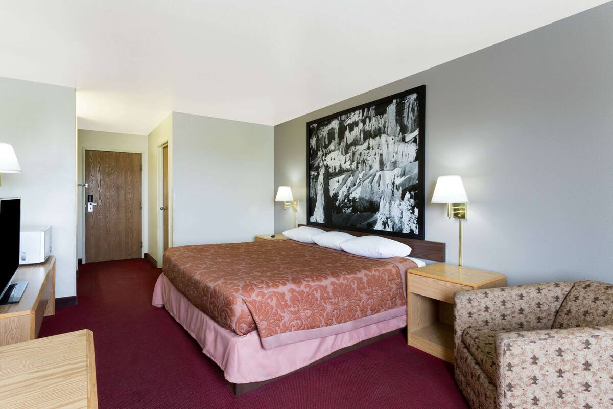 Camera d'albergo con un letto grande, due lampade ai comodini, una TV a schermo piatto, una scrivania in legno, una poltrona con motivo floreale e un quadro astratto di grandi dimensioni appeso al muro.