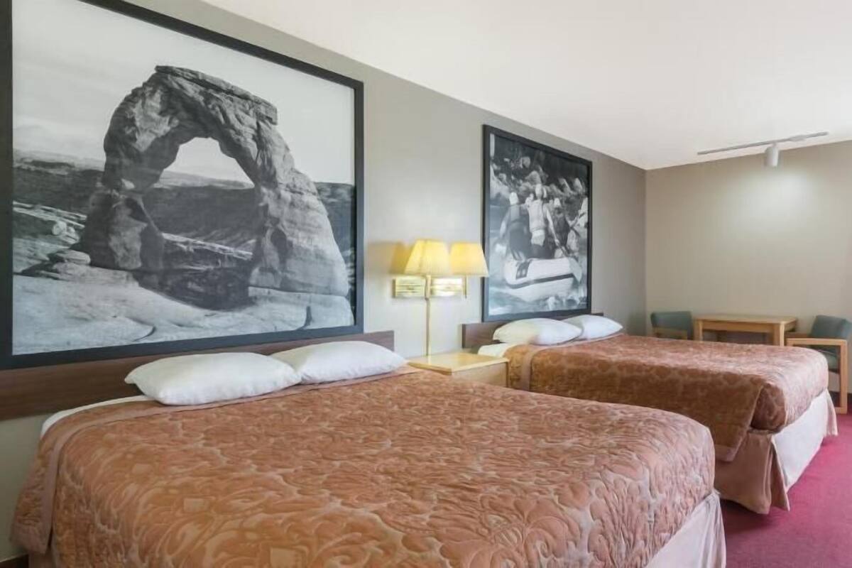Camera d'albergo con due letti, una scrivania, una sedia, una lampada e due quadri appesi al muro.