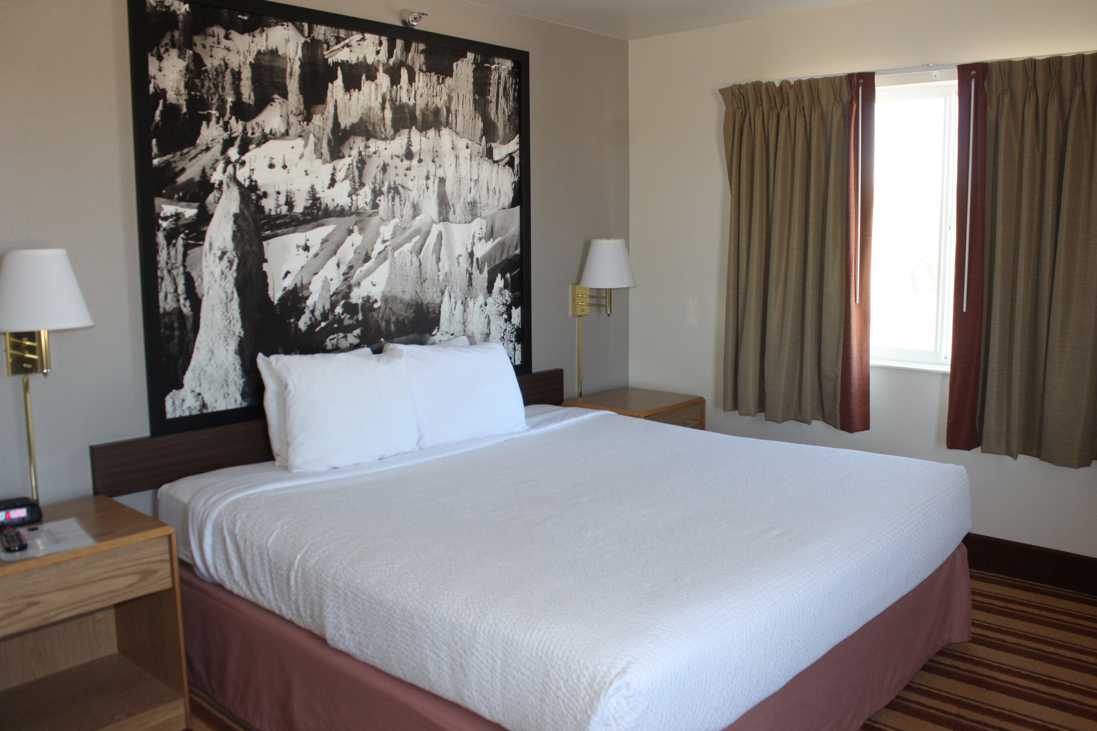 Una habitación de hotel con una cama grande, dos mesitas de noche, una lámpara de pared y una ventana con cortinas.