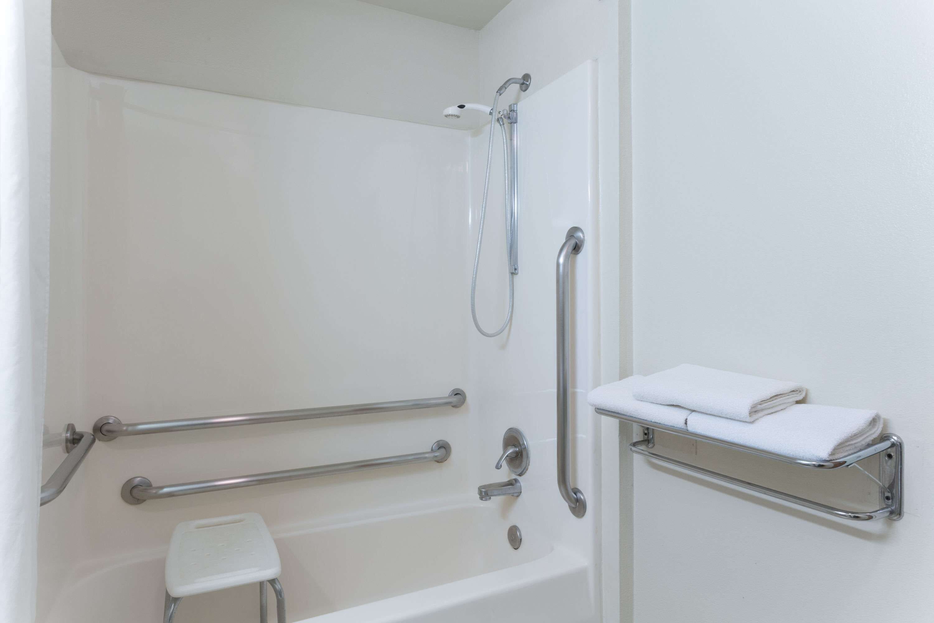 A bathroom with a white bathtub, grab bars, a handheld showerhead, and a towel rack.