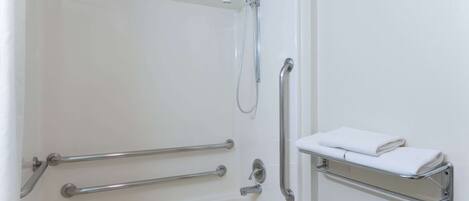Un baño con una bañera blanca, barras de apoyo, un cabezal de ducha manual y un perchero para toallas.