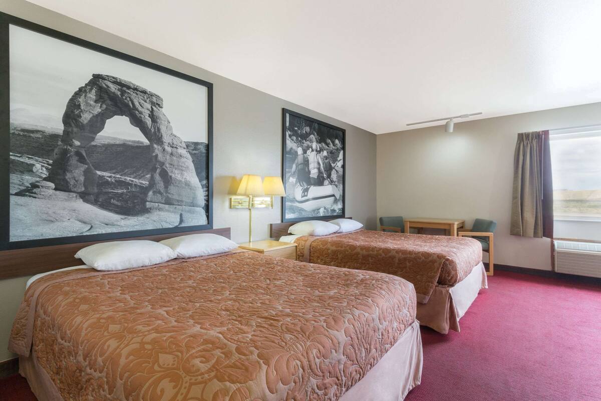 Camera d'albergo con due letti, una scrivania, una sedia e grandi quadri appesi al muro.