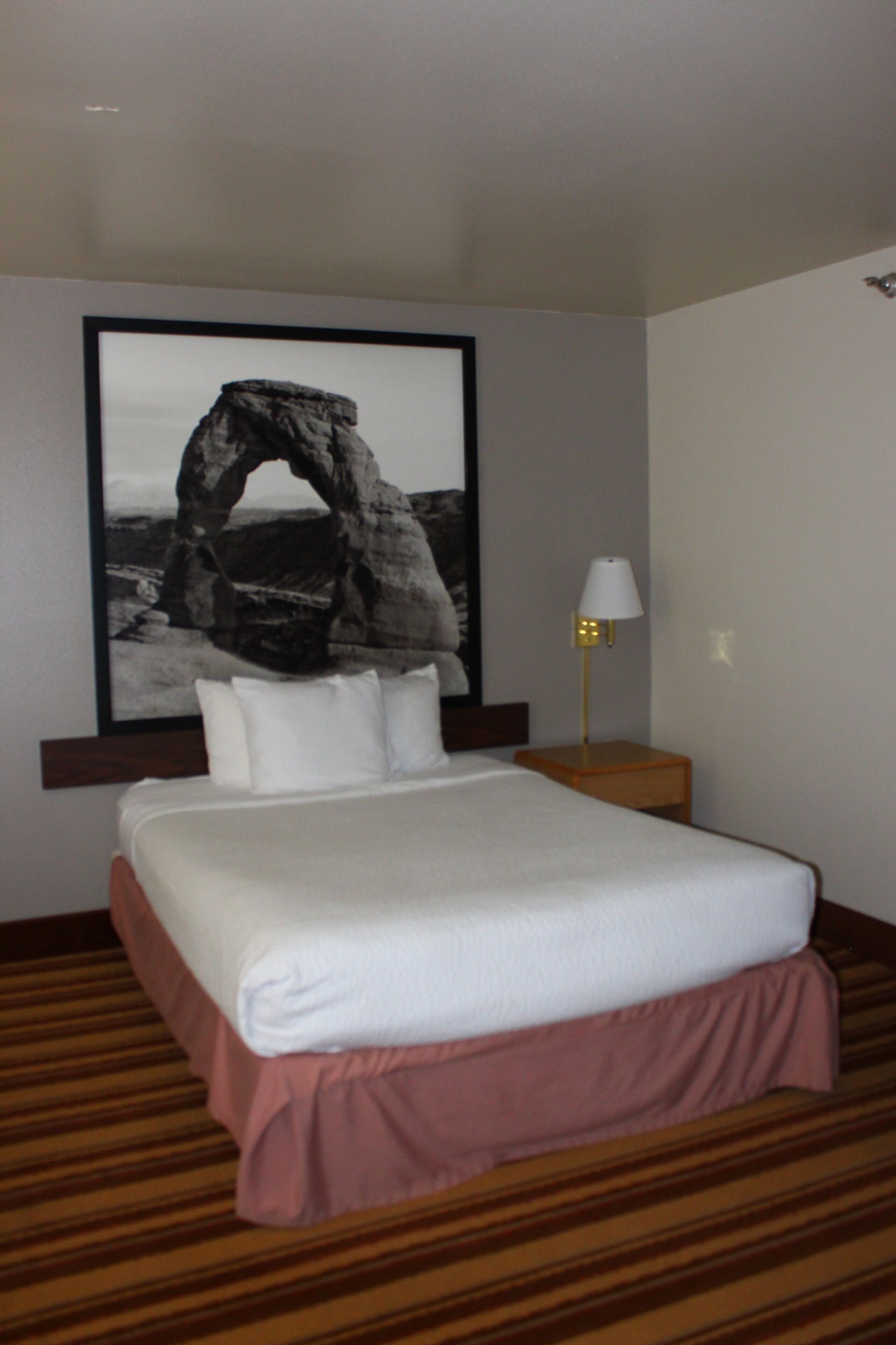 A hotel room with a bed, a nightstand, a lamp, and a framed picture on the wall.