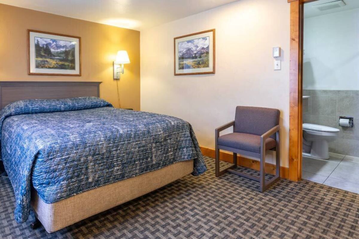 A hotel room with a bed, a chair, a nightstand, and a bathroom visible through an open door.
