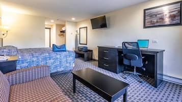 Habitación de hotel con cama, escritorio con computadora, una silla, una mesita y televisor en la pared.