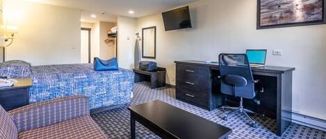 A hotel room with a bed, a desk with a computer, a chair, a small table, and a television on the wall.