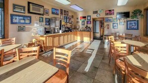 Un restaurante con mesas y sillas de madera, una barra con caja registradora y varias imágenes enmarcadas en las paredes.