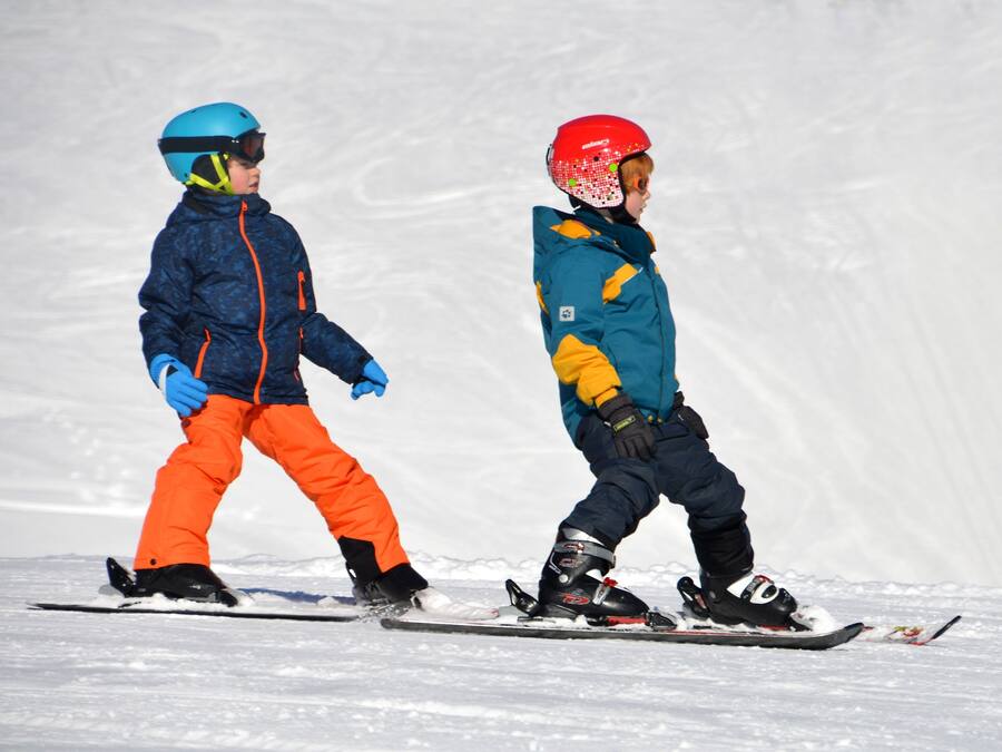 Zwei Kinder mit Ski in verschneiter Landschaft.