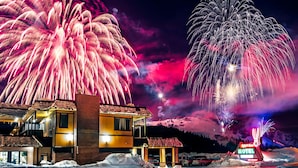Un motel con un letrero de neón, suelo cubierto de nieve y fuegos artificiales al fondo.