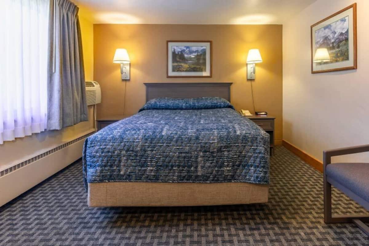 A hotel room with a large bed, two bedside lamps, a chair, and two framed pictures on the wall.
