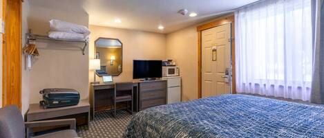 A hotel room with a bed, a desk with a computer, a TV, a microwave, and a door with a curtain.