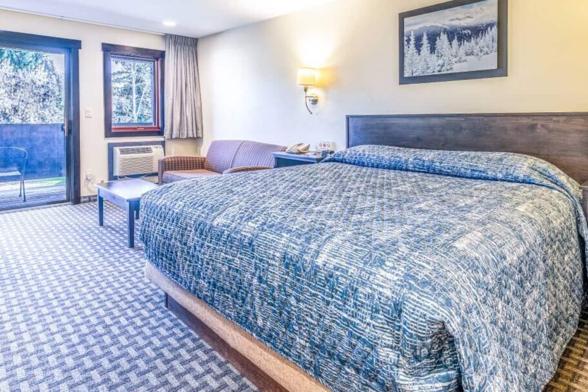 A hotel room with a large bed, a desk, a chair, a window, and a door leading to a balcony.