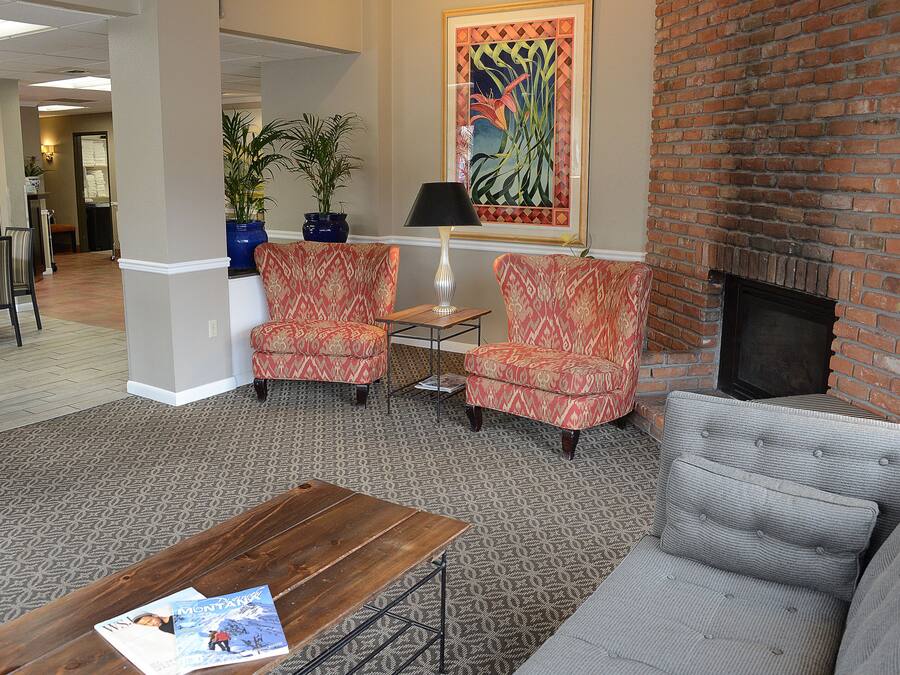 A lobby with a brick fireplace, patterned carpet, and two armchairs.