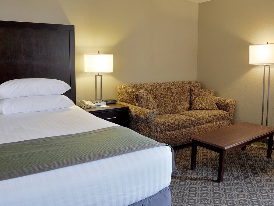 A hotel room with a bed, a patterned armchair, a small table, and two bedside lamps.
