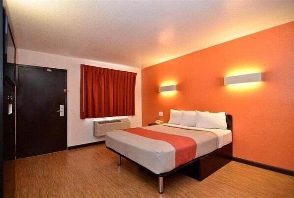 Habitación de hotel con cama, ventana con cortinas, lámpara de pared y puerta.