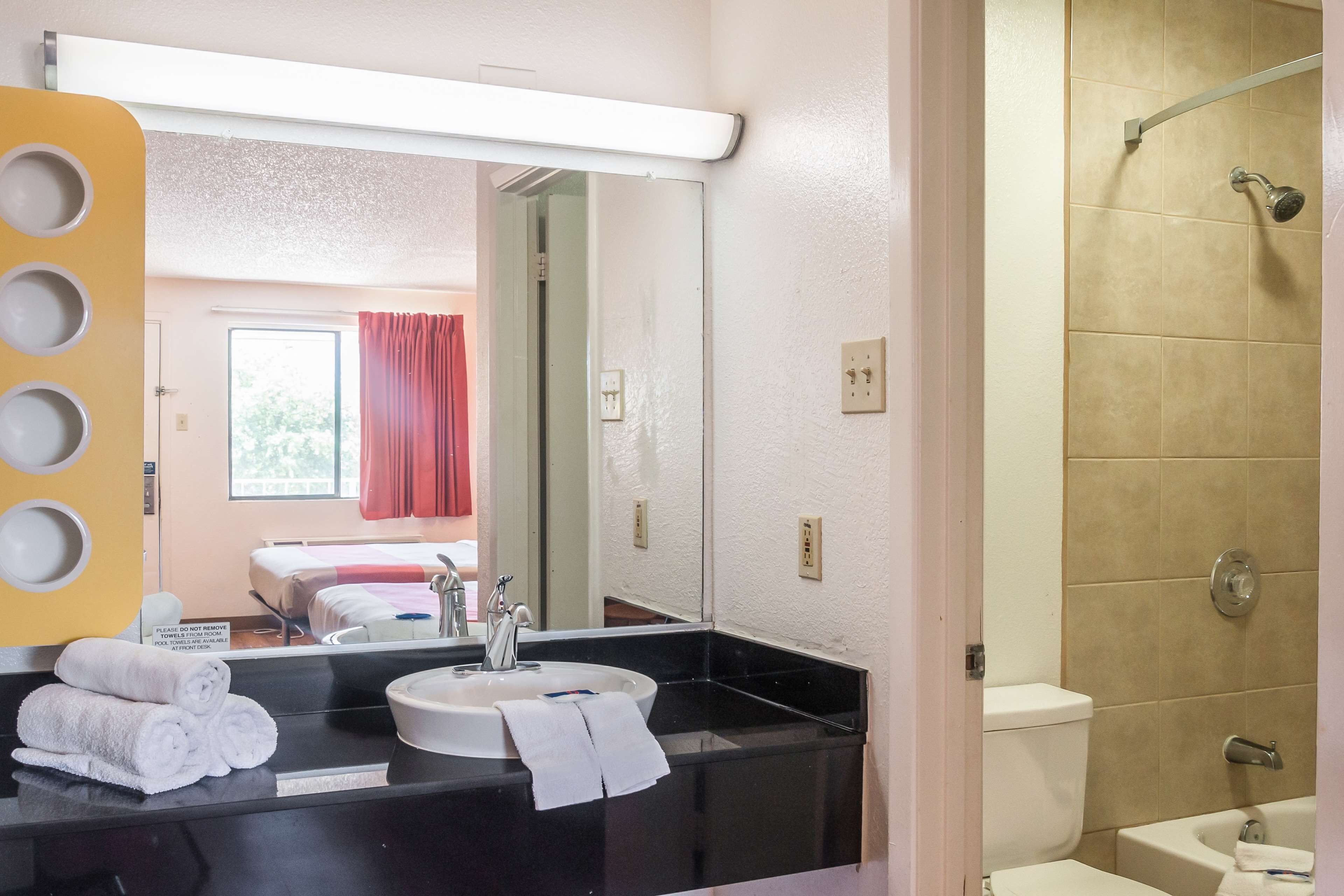 A bathroom with a sink, mirror, and shower. There is a towel rack with towels and a sign on the wall.