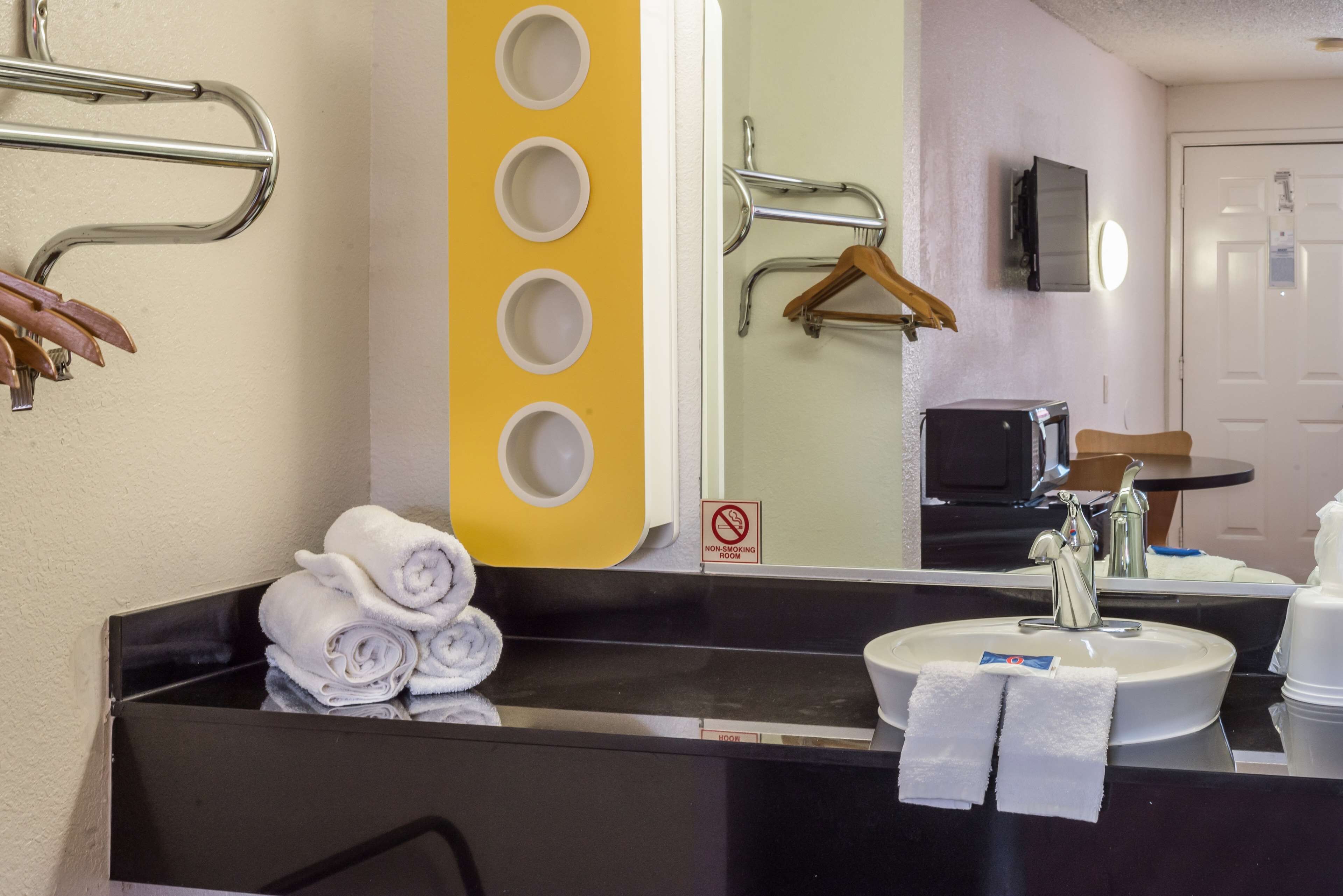 Un baño de hotel con un lavamanos negro, toallas blancas, un espejo y un cartel de prohibido fumar.
