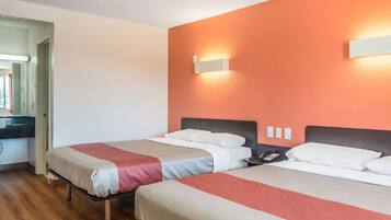 Habitación de hotel con dos camas, piso de madera, baño con espejo y pared de acento roja.