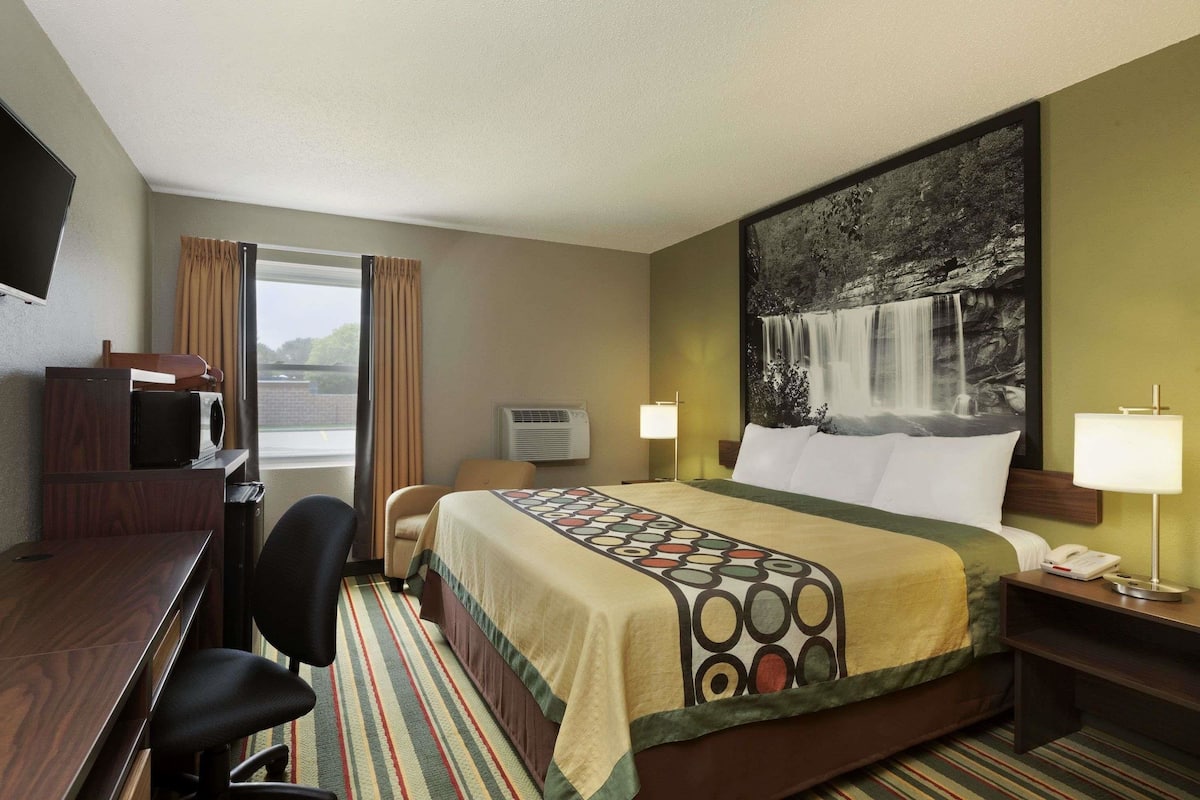 A hotel room with a bed, desk, chair, and a large painting of a waterfall on the wall.