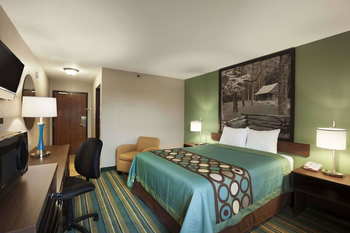 A hotel room with a bed, a desk, a chair, and a television.