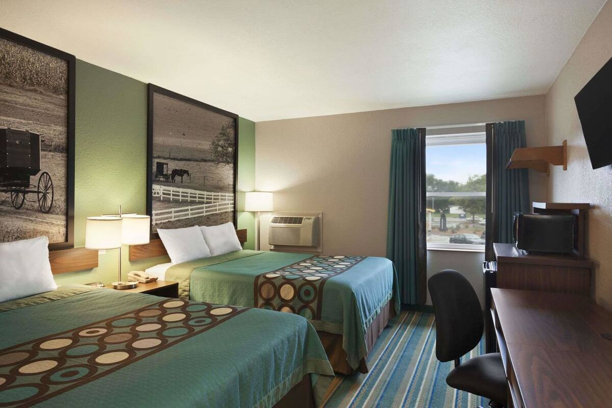 A hotel room with two beds, a desk, a chair, a TV, and a window with curtains.