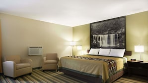 Une chambre d’hôtel avec un grand lit, deux fauteuils, une table de chevet avec une lampe et un climatiseur fixé au mur.