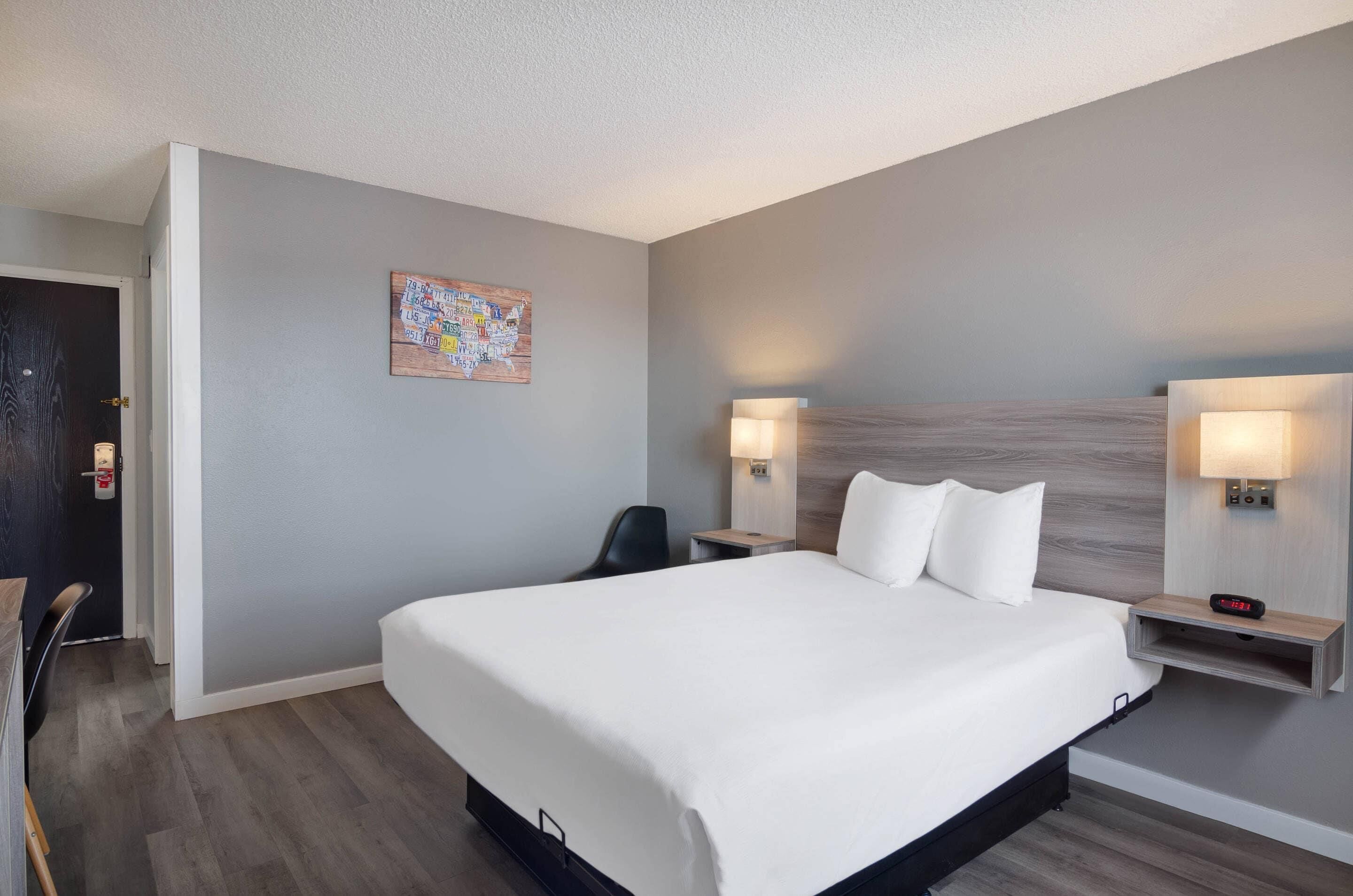 A hotel room with a large bed, two bedside tables with lamps, a chair, and a wall-mounted clock.