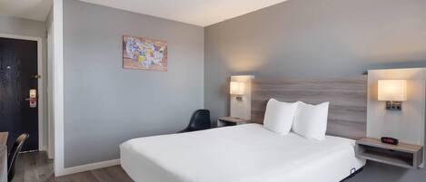 A hotel room with a large bed, two bedside tables with lamps, a chair, and a wall-mounted clock.