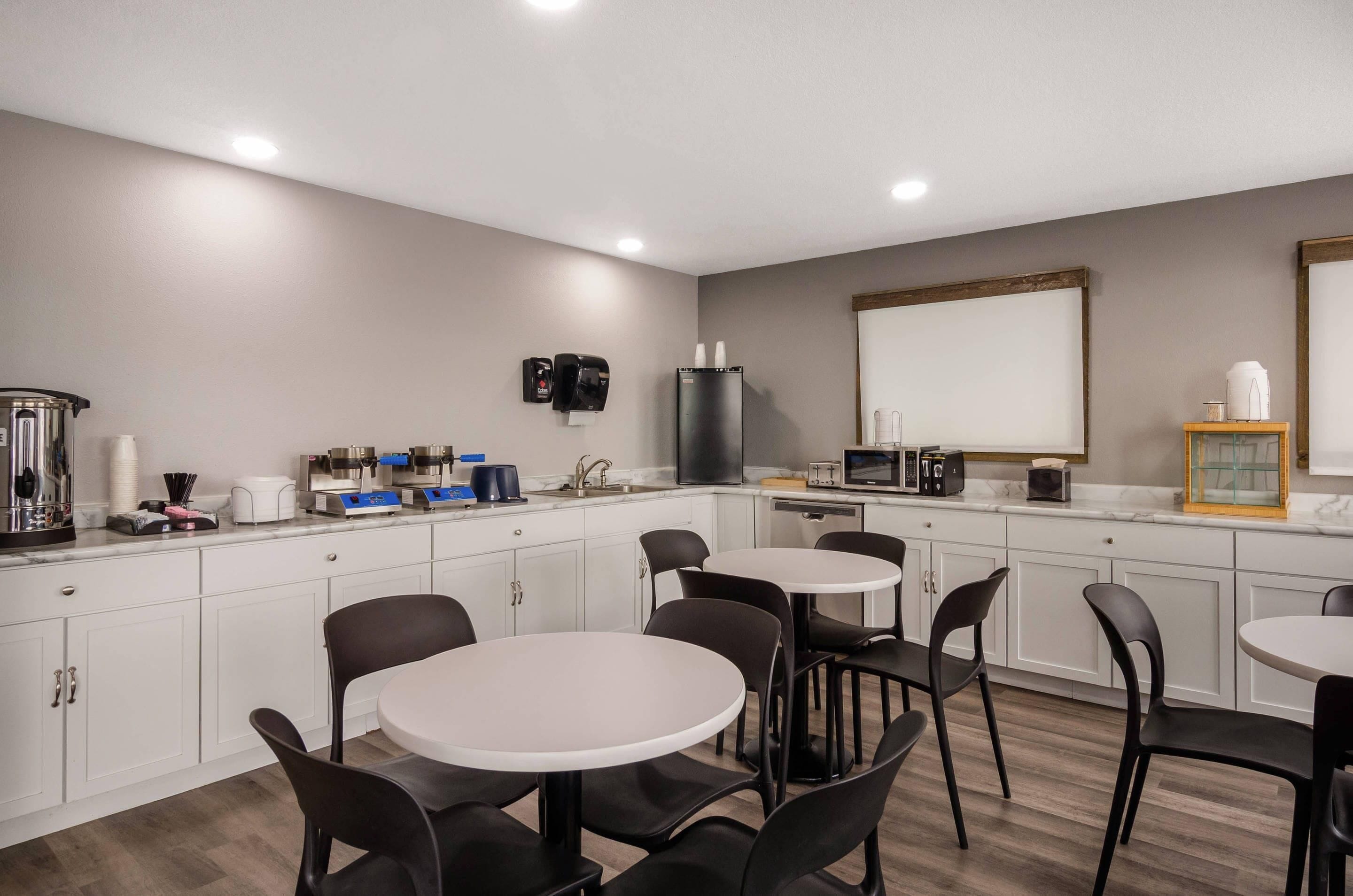 Een moderne keuken met witte kasten, een inbouwoven en een koffiehoek. Er staan twee ronde tafels met stoelen.