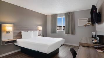 A hotel room with a large bed, bedside tables with lamps, a desk with a chair, a television mounted on the wall, and a window with curtains.
