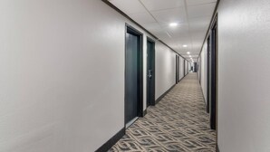 Un long couloir étroit, doté d’un tapis à motifs, de murs blancs et de portes d’un seul côté.