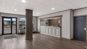 Un espace d’accueil avec un comptoir de réception en bois, un coin salon avec des chaises et une grande porte donnant sur la rue.
