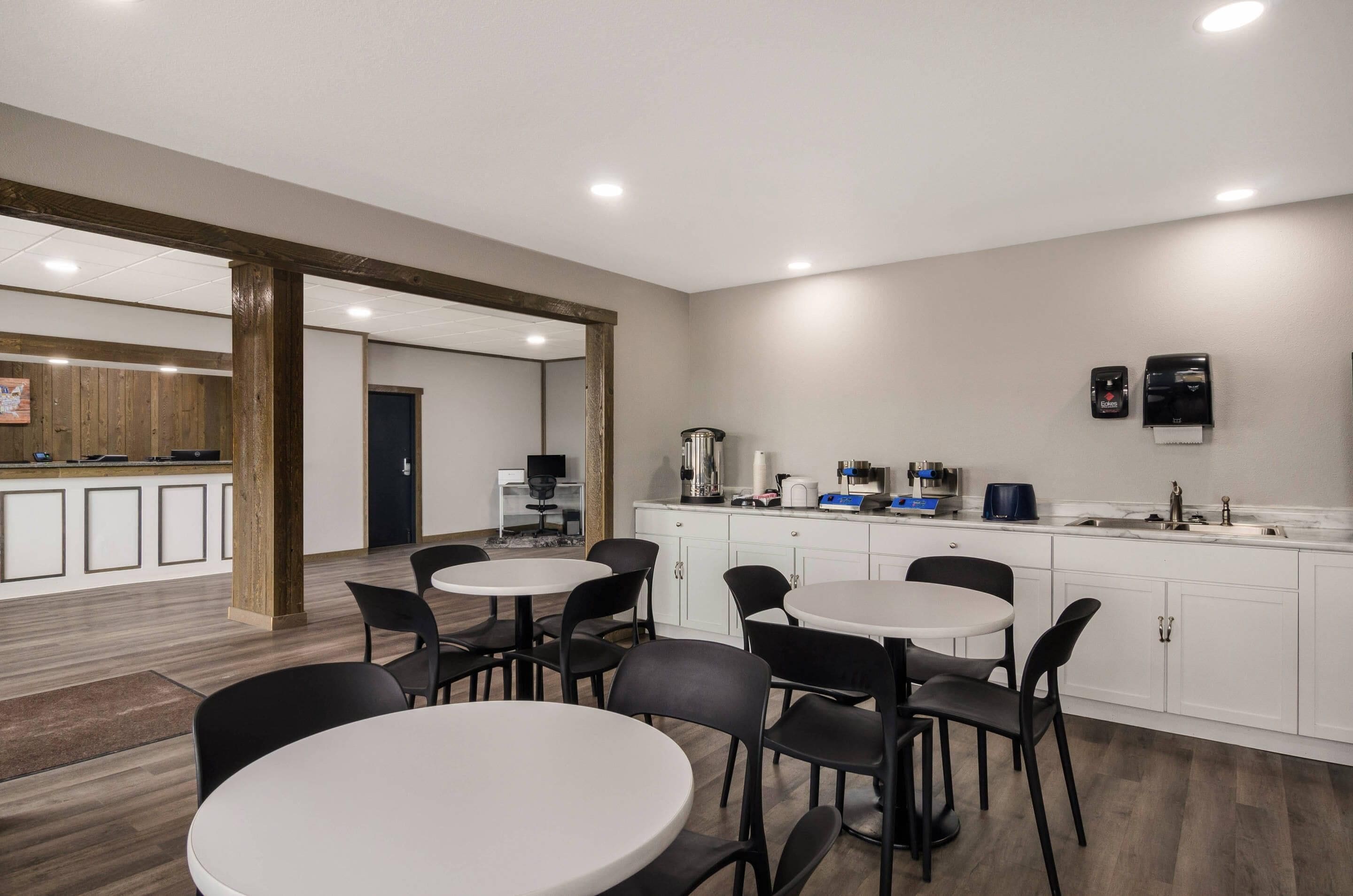 Une cuisine moderne avec des meubles blancs, un évier et une machine à café. On y trouve plusieurs tables et chaises rondes dans l’espace repas.