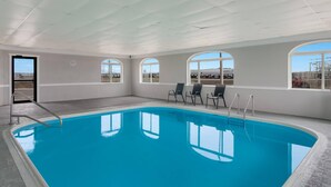 Une piscine intérieure avec de grandes baies vitrées offrant une vue dégagée, une horloge au mur et une porte donnant sur l’extérieur.