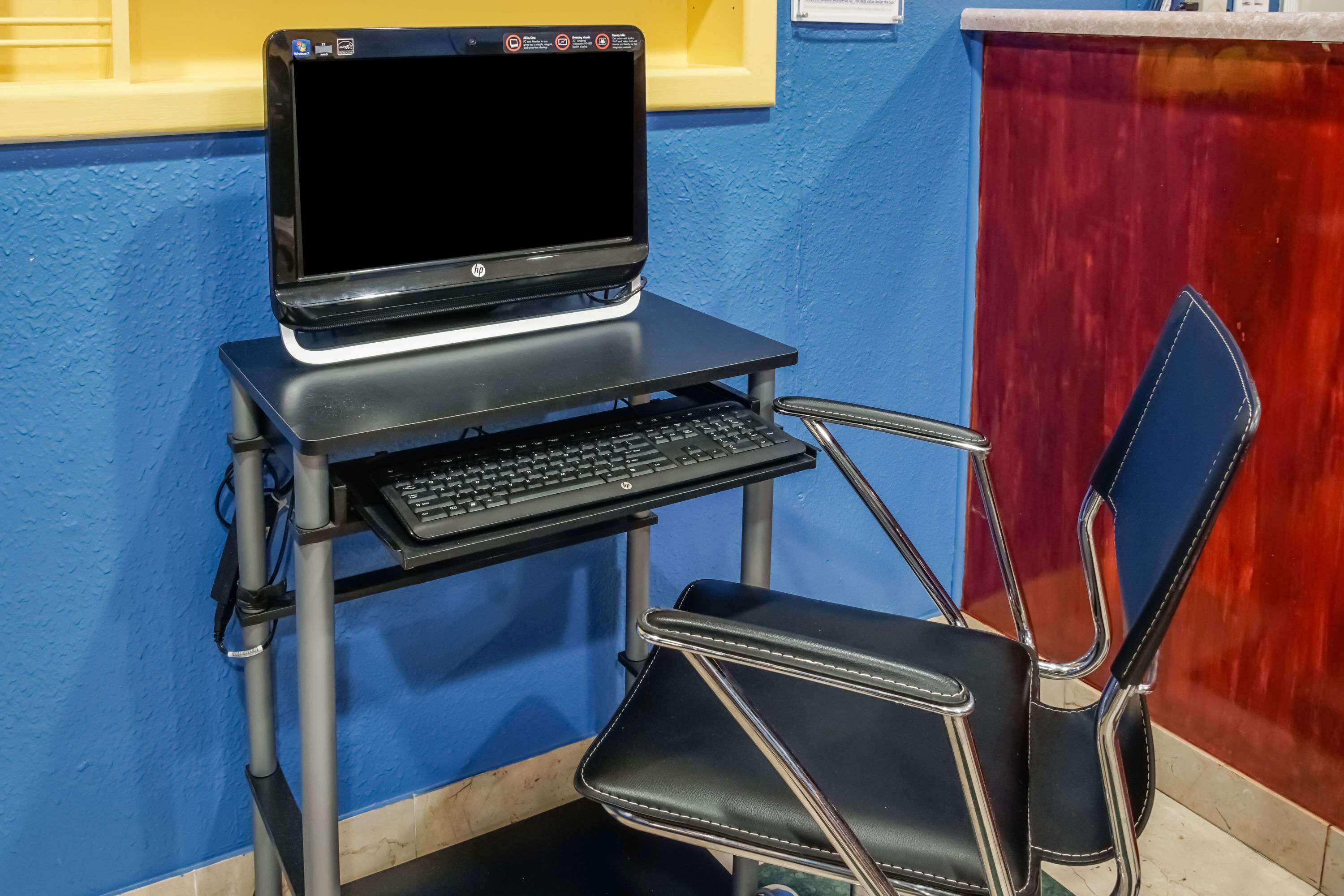 A laptop on a portable desk with a keyboard, a black chair, and a blue wall.
