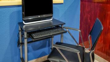 A laptop on a portable desk with a keyboard, a black chair, and a blue wall.