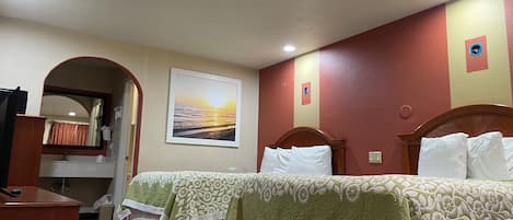 A hotel room with two beds, a desk, a mirror, and a framed picture on the wall.