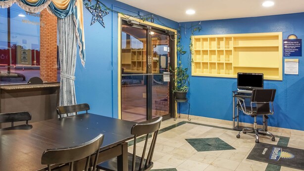 A conference room with a long table and chairs, a computer on a desk, and a window with curtains. - Days Inn by Wyndham Bastrop (Bastrop)