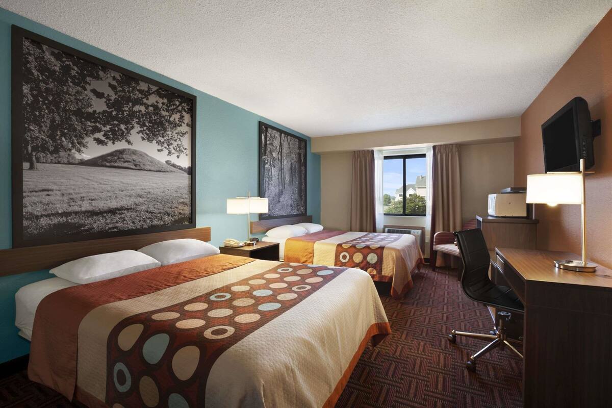 A hotel room with two beds, a desk, a chair, and a TV.