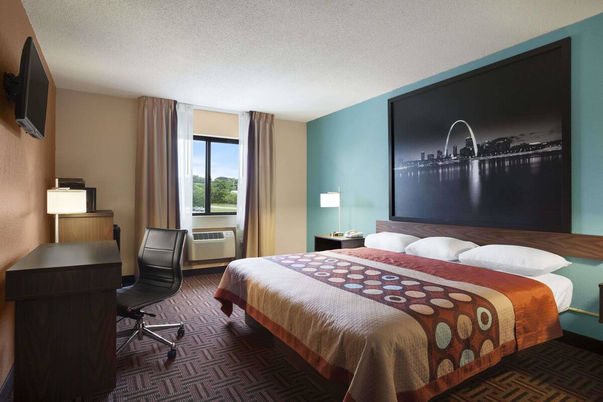 A hotel room with a bed, a desk, a chair, a TV, and a large window.