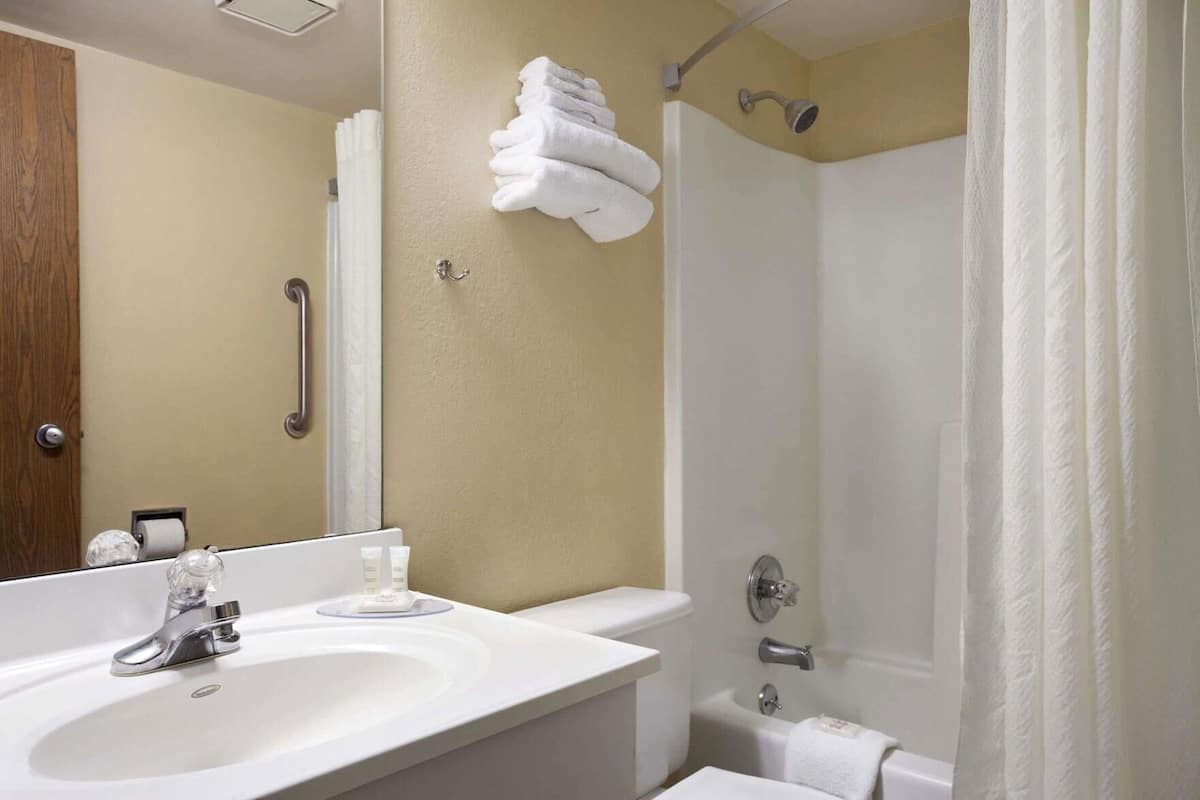 A bathroom with a sink, mirror, towel rack, shower, and toilet.