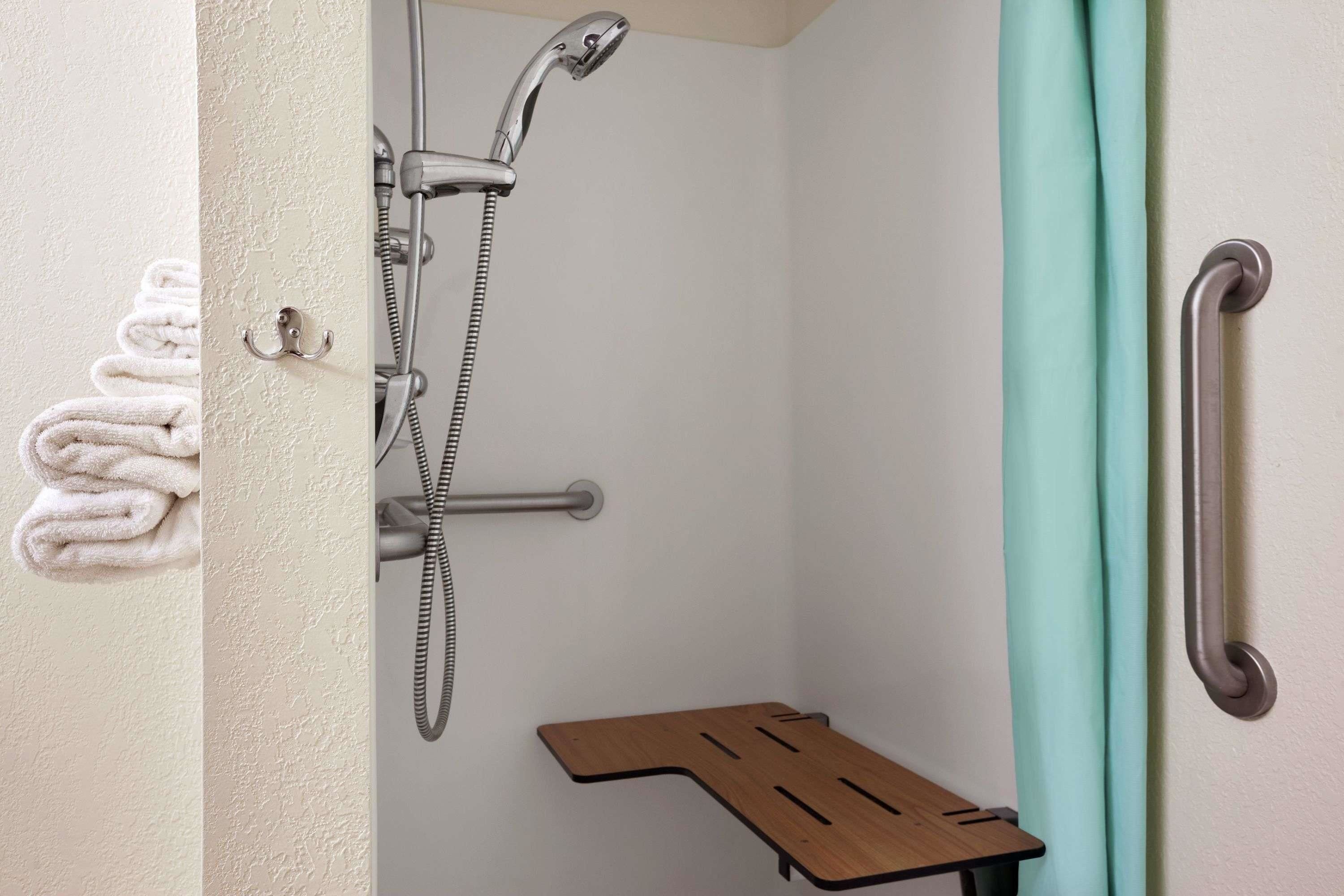 Une salle de bain équipée d’une douche, d’un porte-serviettes, d’une barre d’appui et d’une étagère en bois.