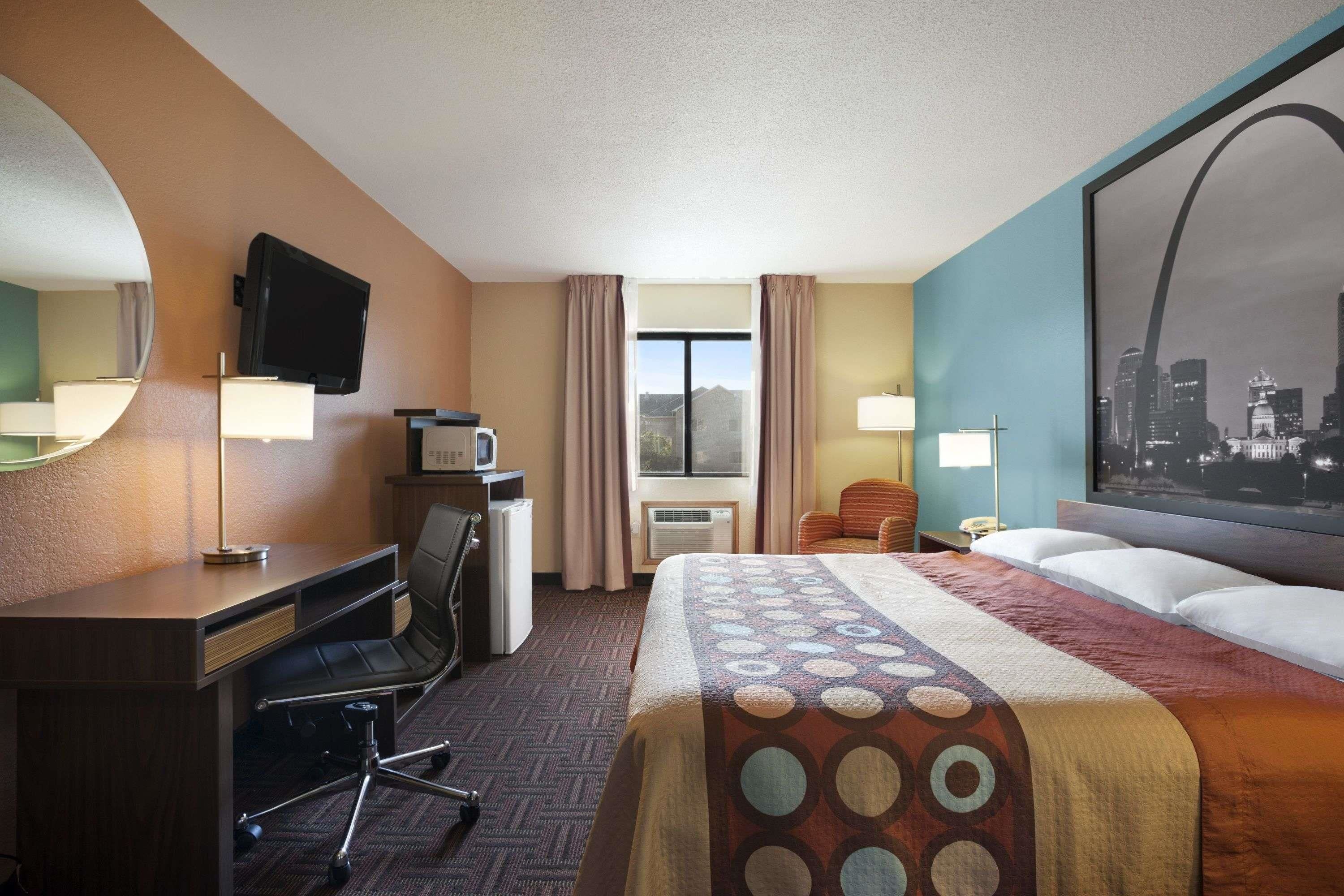 A hotel room with a bed, desk, chair, TV, air conditioning unit, and a large window.