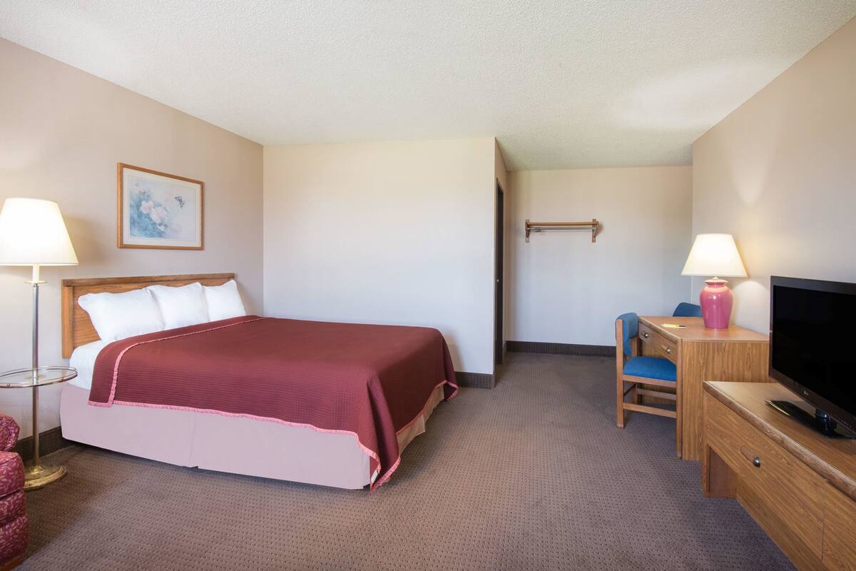 A hotel room with a bed, a desk, a chair, a TV, and a lamp.